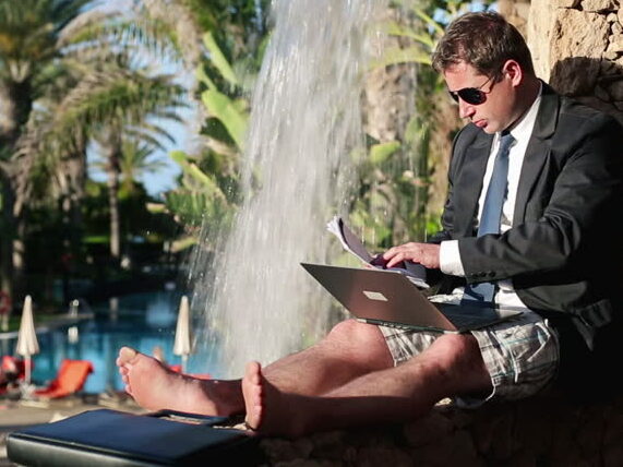 Business man en costard cravate, pc portable sur les genoux, en short et paysage de vacances.